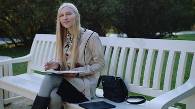 美丽的女人坐在板凳上秋天公园使<strong>笔记笔记</strong>本